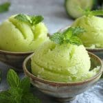 Tre skålar med gurksorbet toppad med färsk mynta, omgiven av gurkskivor.