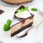 En bit cheesecake med mintchoklad, toppad med grädde och mynta på en vit tallrik.