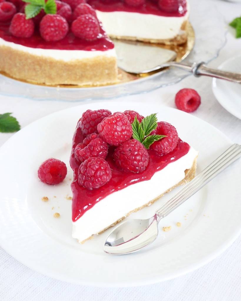 Jordgubbscheesecake 9 En bit halloncheesecake med färska hallon och bär på en vit tallrik.