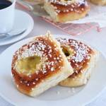 Två kanelbullar med vaniljkräm och pärlsocker på en tallrik bredvid en kopp kaffe.