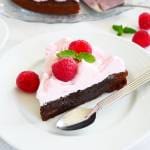 En bit kladdkaka med hallonmaräng, dekorerad med hallon och mynta på en vit tallrik.