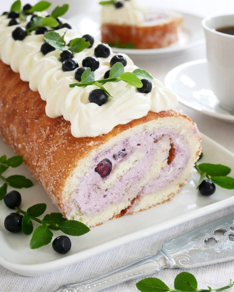 Blåbärsbullar med citron 10 Blåbärsrulltårta dekorerad med grädde, blåbär och mynta på en tallrik.