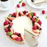 Cheesecake dekorerad med jordgubbar, hallon, blåbär och mynta på en glasskiva.