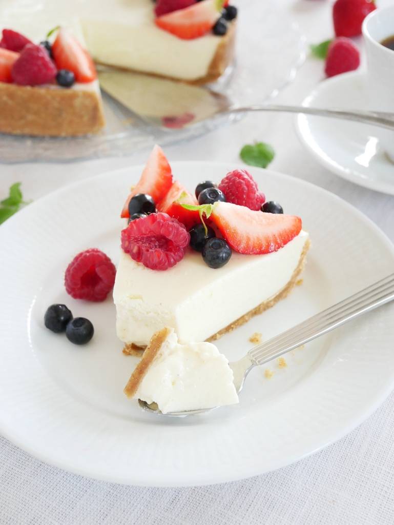 Jordgubbscheesecake 10 En bit cheesecake med bär, inklusive jordgubbar, hallon och blåbär, på en vit tallrik.