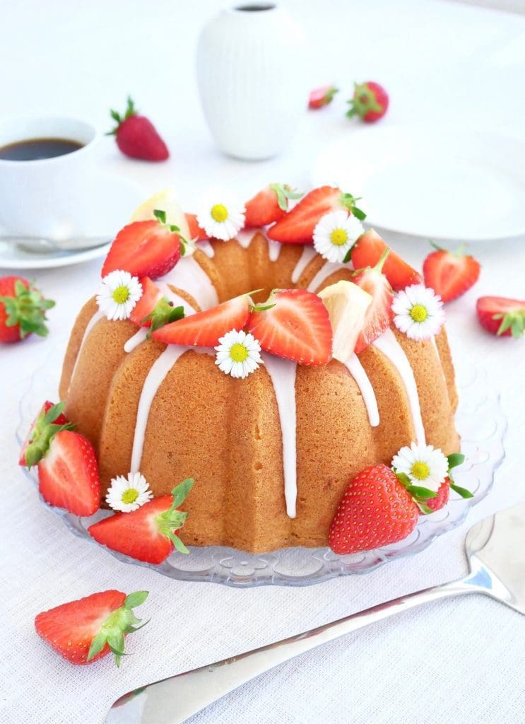 Saftig hallonkaka 8 Fläder sockerkaka dekorerad med jordgubbar och små blommor på en glasskiva.