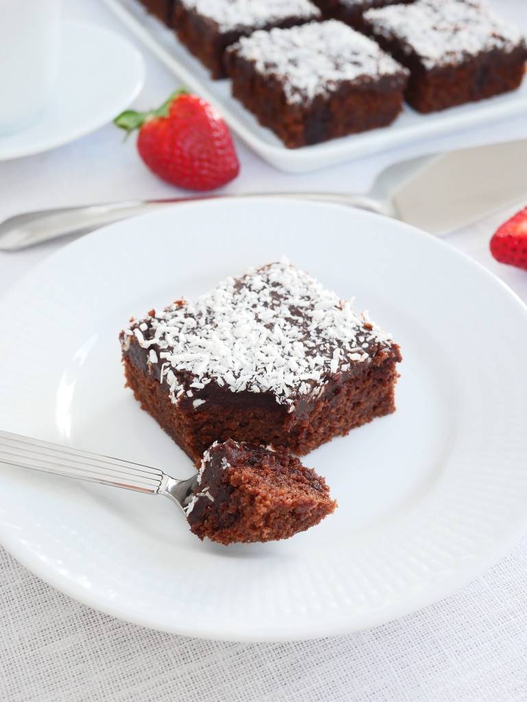 Rabarbermums 10 En bit kärleksmums med chokladglasyr och kokosflingor på en vit tallrik med en gaffel.