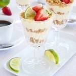 Key lime pie serverad i glas med jordgubbar och lime på en vit tallrik.
