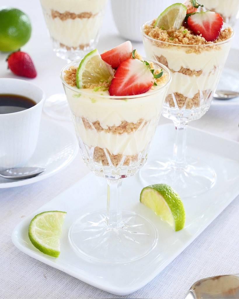 No bake daimpannacotta-rutor 11 Key lime pie serverad i glas med jordgubbar och lime på en vit tallrik.
