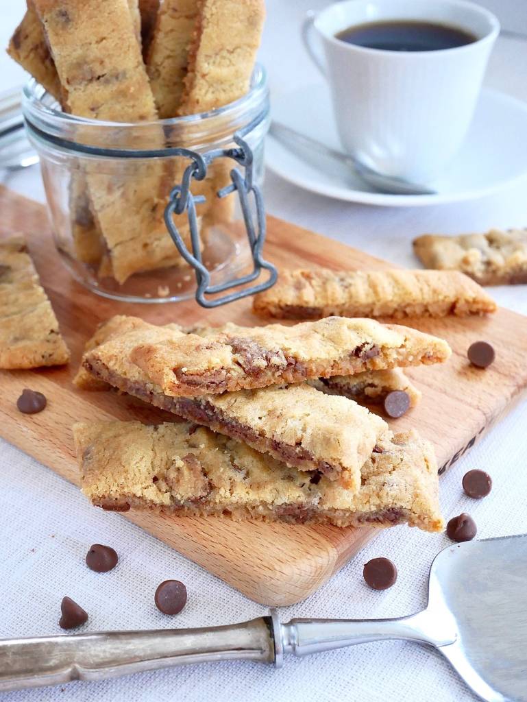Rabarbersnittar 11 Kolasnittar med mjölkchoklad på en skärbräda med en kopp kaffe i bakgrunden.