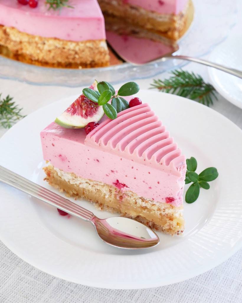 No bake blåbärscheesecake 9 En bit lingoncheesecake med rosa fyllning, garnerad med fikon och gröna blad på en vit tallrik.
