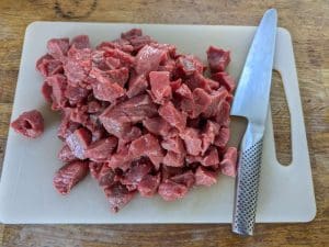 Köttbitar i olika storlekar placerade på en skärbräda bredvid en kökskniv.