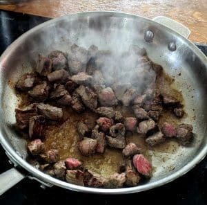 Bitar av kött som steks i en panna med ånga som stiger upp.