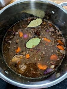 Köttgryta med kött, morötter, lök och lagerblad i en kastrull.