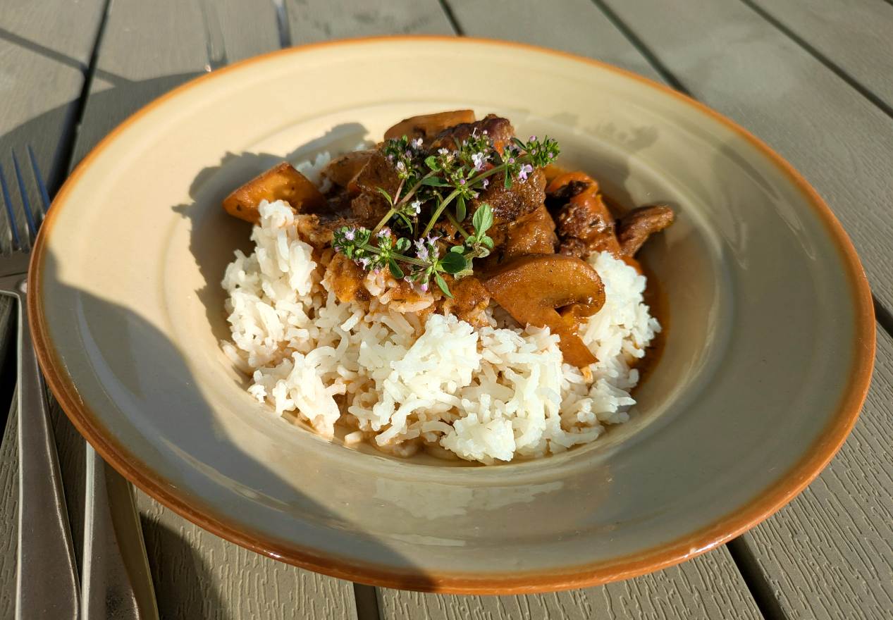 Kebabgryta 5 En skål med ris och köttgryta toppad med örter på en träyta.