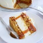 En bit morotscheesecake med karamellsås på en vit tallrik med en sked.