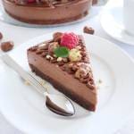 En bit nutellacheesecake med hallon och nötter på en vit tallrik med gaffel.