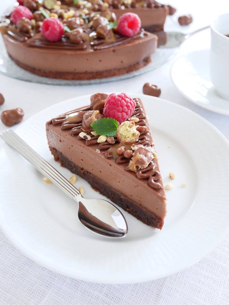 Påskkaniner med Nutella 6 En bit nutellacheesecake med hallon och nötter på en vit tallrik med gaffel.