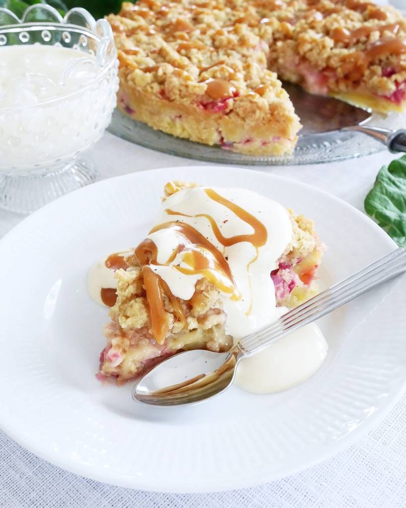 Citronkladdkaka med vit chokladpannacotta 13 En bit rabarberkladdkaka serverad med grädde och sås på en vit tallrik.