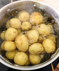 En kastrull med kokande potatisar som sjuder i vatten på en spis.