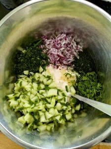Skål med hackad gurka, rödlök, gräslök och sås i en metallskål.