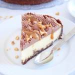 En bit snickers cheesecake med chokladfrosting och kolasås på en vit tallrik.