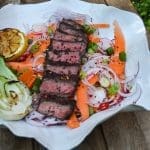 Grillad biff skivad och serverad med grönsaker och sallad på en vit tallrik.