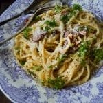 En tallrik med spaghetti, parmesanost och persilja på en blå och vit mönstrad tallrik.