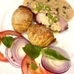 En tallrik med ankbröst, hasselbackspotatis och grönpepparsås, dekorerad med grön lök.