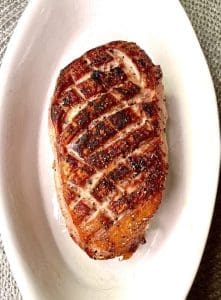 Grillad anka med grillränder i en vit skål på en grå yta.