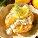 Bakad potatis toppad med skagenröra och citronskivor på en tallrik.