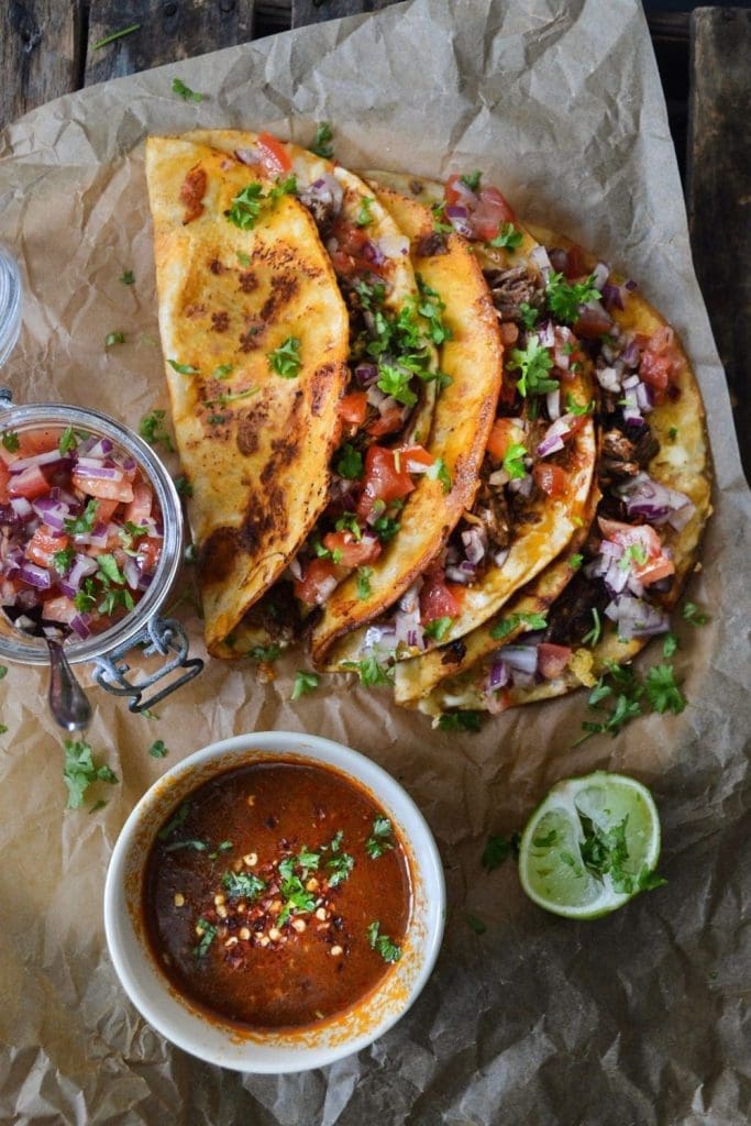 Vit pizza med tryffel 7 En tallrik med birria-tacos serverad med salsa och lime på en pappersunderlag.