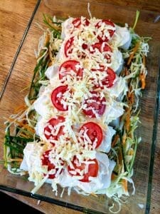 Färsk torskrygg med grönsaker, tomater och riven ost i en ugnsform.