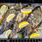 Grillad havsabborre på en plåt med citronskivor och örter.