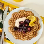 En tallrik med våfflor toppade med bär och citronskivor, serverad med grädde.