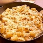 En skål med kycklingpasta toppad med riven parmesanost och örter.