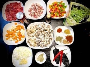 Blandade ingredienser för långkokt chili, inklusive högrev, grönsaker och kryddor.