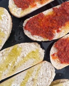 Brödskivor med röd n'duja och grön olivolja på en svart platta.