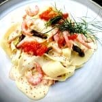 En tallrik med öppen lasagne toppad med lax, räkor och Sandefjordssås.