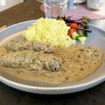 Två oxrullader i gräddsås serverade med ris och en grönsallad på en tallrik.