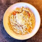 En skål med pasta, sås, körsbärstomater och riven ost på toppen.