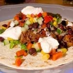 Taco fylld med pulled pork, grönsaker, och gräddfil på en tortilla.