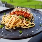 Tallrik med tomatbaserad pasta och hummer, dekorerad med persilja och parmesan.