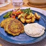 Zucchini- och morotsbiffar serverade med potatis och sås på en blå tallrik.