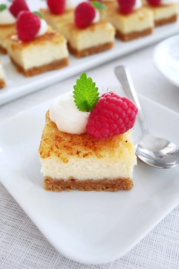 Hallonrutor 8 En bit cheesecake med hallon och grädde på en vit tallrik.