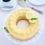 En rund citronkaka med skivor av citron och myntablad på ett fat.