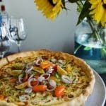 Pizza med en krispig kant, toppad med tomater och lök på en tallrik.