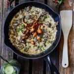 Svart stekpanna med köttsås, kantareller och grädde på en träyta.