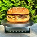 Hamburgare med sesambröd, kött, ost, ketchup och gurka på en svart platta.