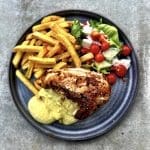 En tallrik med grillad kyckling, pommes frites, sås och en sallad med tomater och grönsaker.