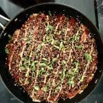 En stekpanna med okonomiyaki toppad med köttfärs, sås och grönsaker.